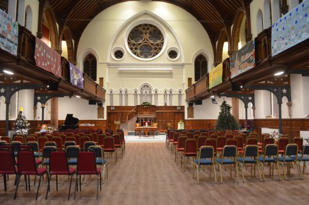 The illuminated inside of a church, showing the alter and seating.